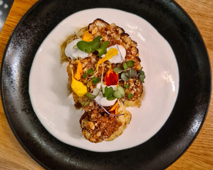 cauliflower covered in fresh herbs on a black plate