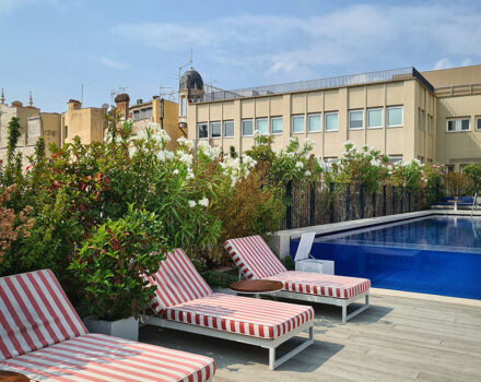 outdoor swimming pool with striped red and white sunloungers and a blue sky